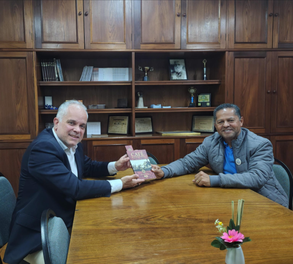 Presidente da Academia Nacional de Economia recebe do Presidente da ACIAR a obra "Historia do Café", simbolizando o intercâmbio institucional e a valorização da memória econômica regional.